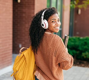 A young woman smiles back at the camera as she walks on a college campus.