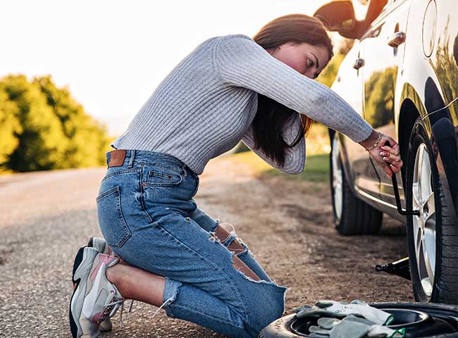 Young woman confidently changes her car tire, thankful her emergency fund can help cover costs.