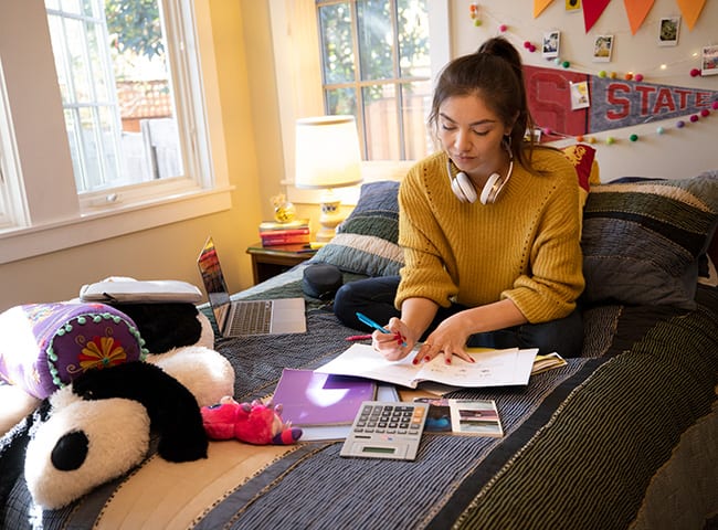 A student completes homework on her bed.