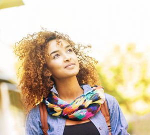 A young woman wearing a scarf stares into the distance outside