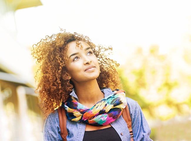 A young woman wearing a scarf stares into the distance outside