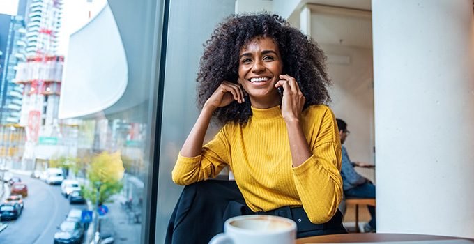 A recent grad smiles and talks on the phone in a coffee shop.