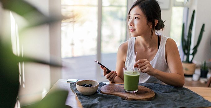 A freelancer sits in her home with a green smoothie.